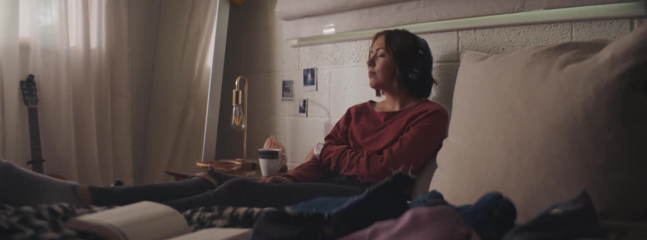 A woman is lying in bed and listening to something on headphones