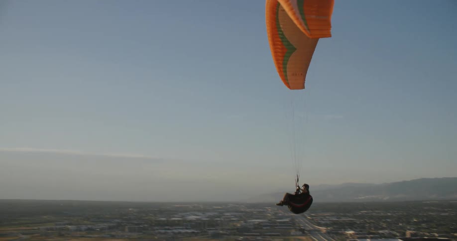 A person paragliding over a rural city in the morning