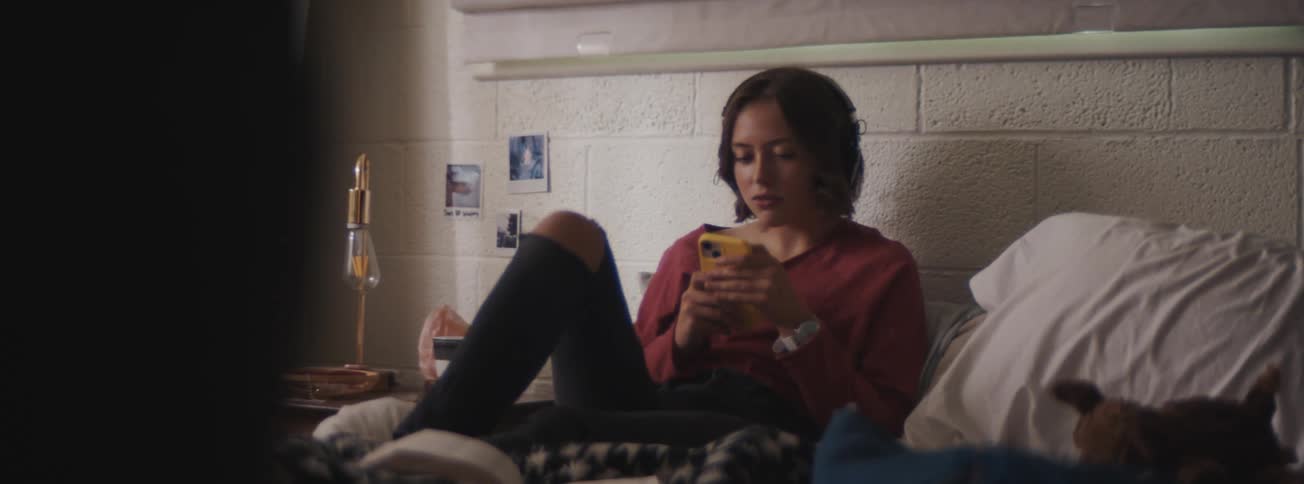 A woman sitting on a bed and talking to someone on her cell phone