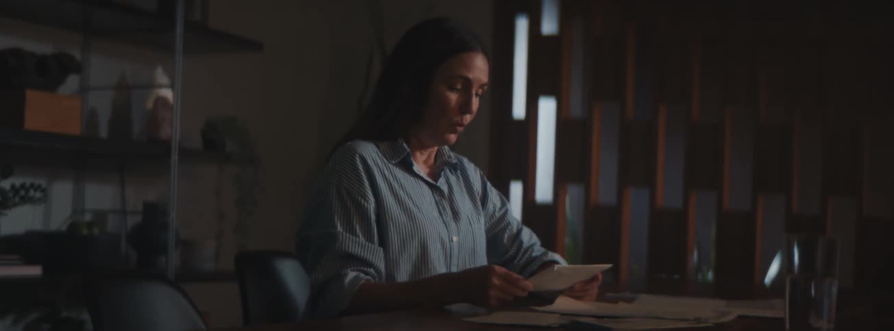 A woman sitting at a desk looking worried as she goes through bills