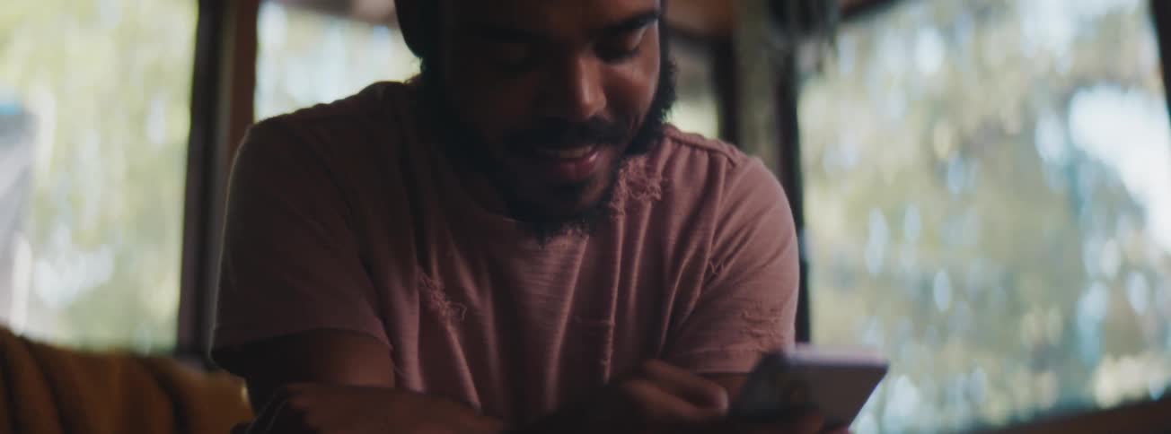A man smiling while pressing mobile phone indoor at midday