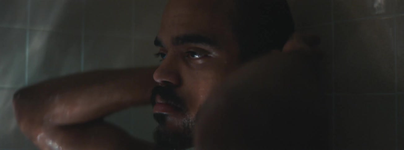 A sad man with a beard is taking a shower and has a tired expression