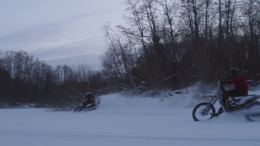 Two motorcyclists ride through freshly fallen snow and spit up snow behind them