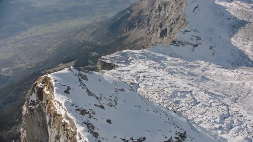 A rocky mountain ridge is covered in a layer of snow on a sunny day