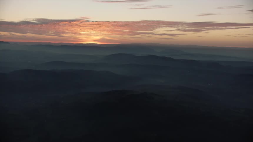 The sun is just below the horizon behind a sprawling mountain range