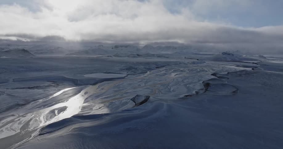 Aerial view of a river in the tundra under white clouds