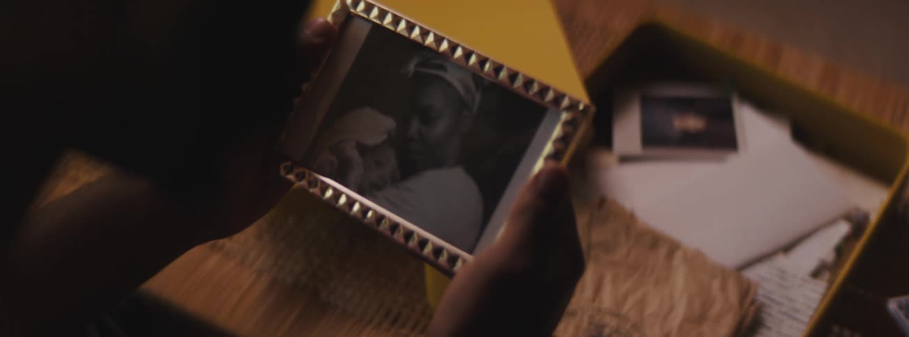 A man reads a letter and pulls a framed photograph out of a box before stroking it from a memory box