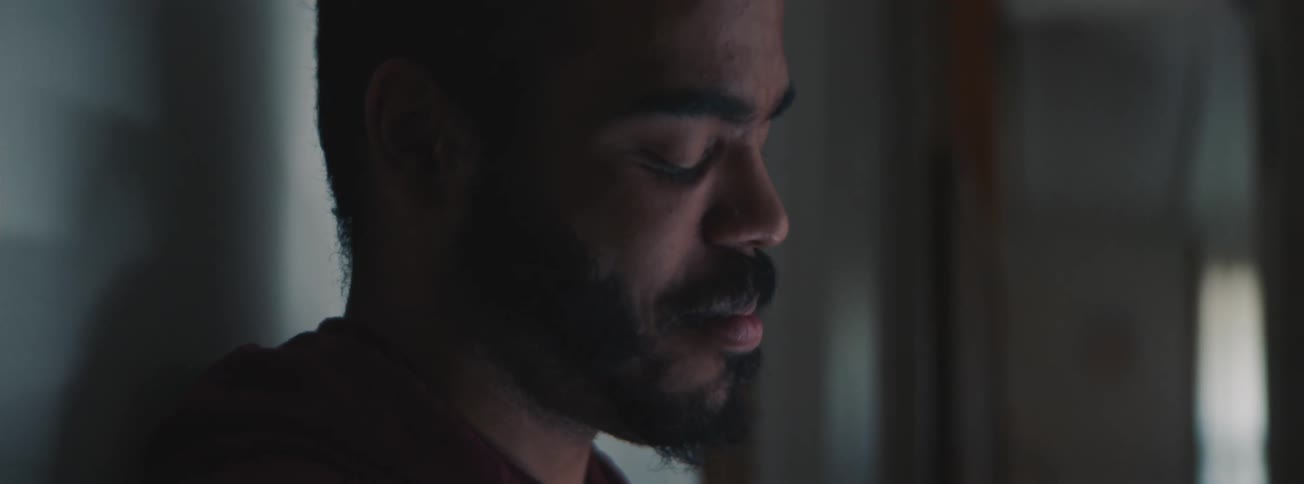A man with his back against the wall smiling while looking down at a laptop