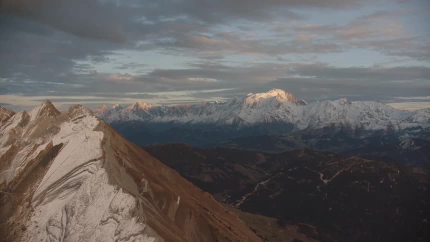 Aerial panorama of a mountain range covered by snow in a sky with morning clouds