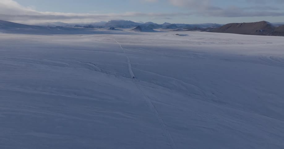 Big rig drives across a flat snow covered terrain near mountains at dusk