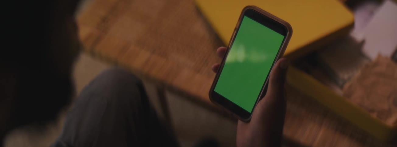 A hand holding a smart phone displaying a green screen