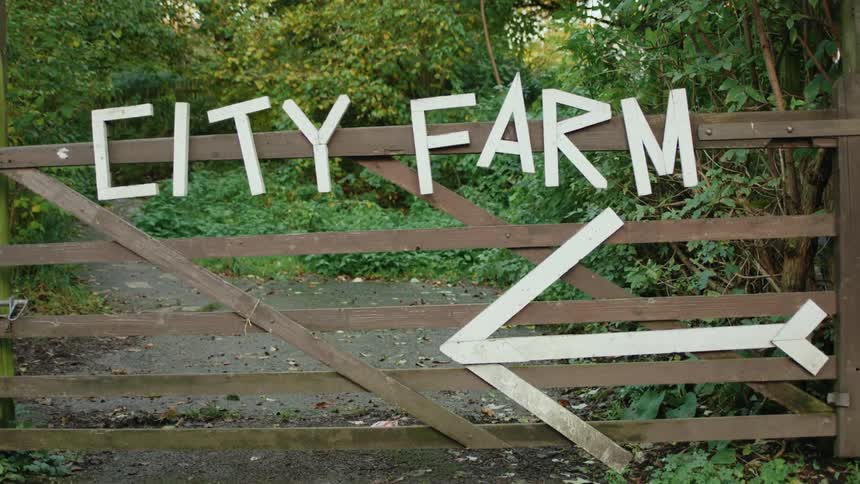 A handmade gate and signage pointing toward a city farm in a rural area during the day