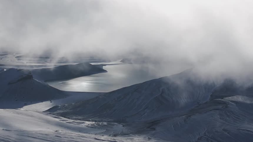 Aerial panorama of icecovered mountains with a lake at cloud level