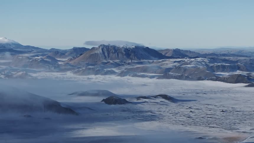 Snow covers plains between mountains on a foggy day