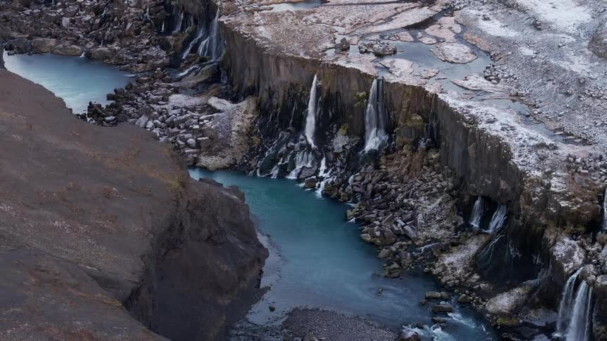 Aerial of a waterfall falling from a rocky mountain into a river