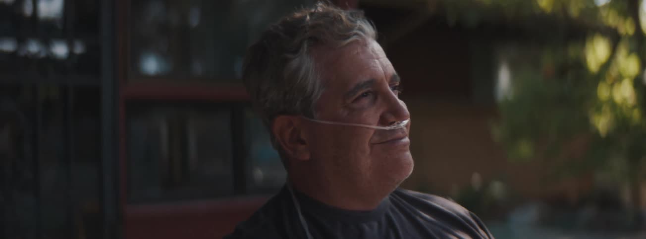 A senior man with an oxygen tube in his nose looking straight ahead and smiling