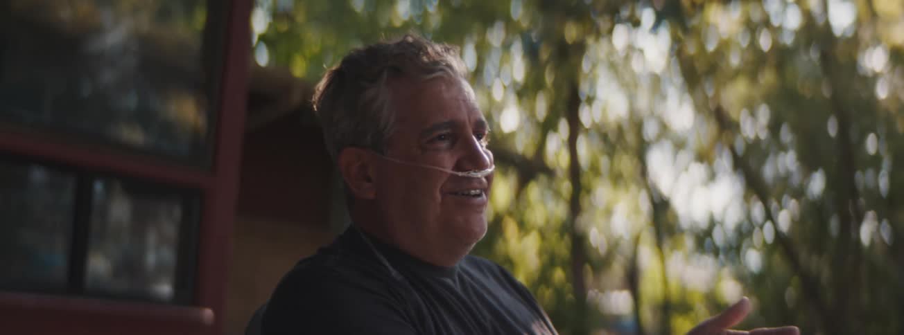 Older man wearing nasal oxygen tubing gestures while talking animatedly