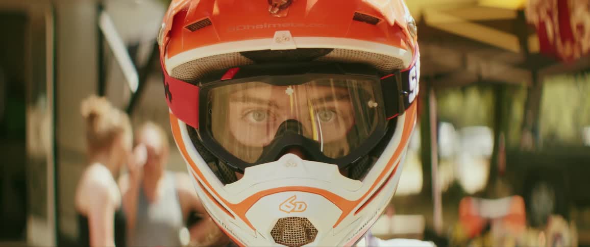 Person wearing crash helmet stands outside building on a sunny day