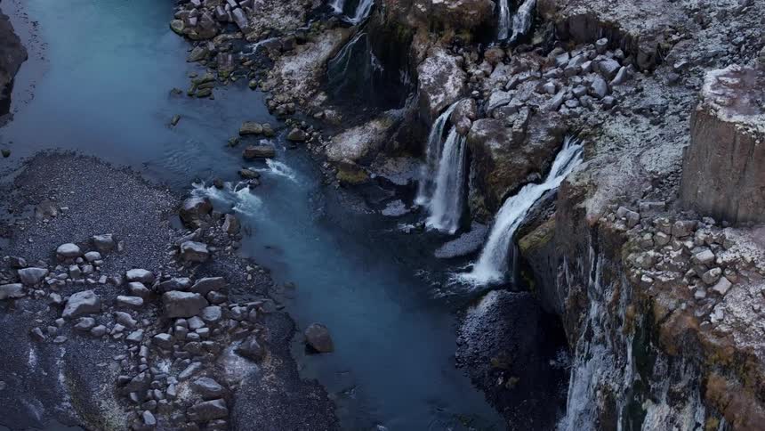 Aerial of a rocky cliff with waterfalls beside a river after sundown