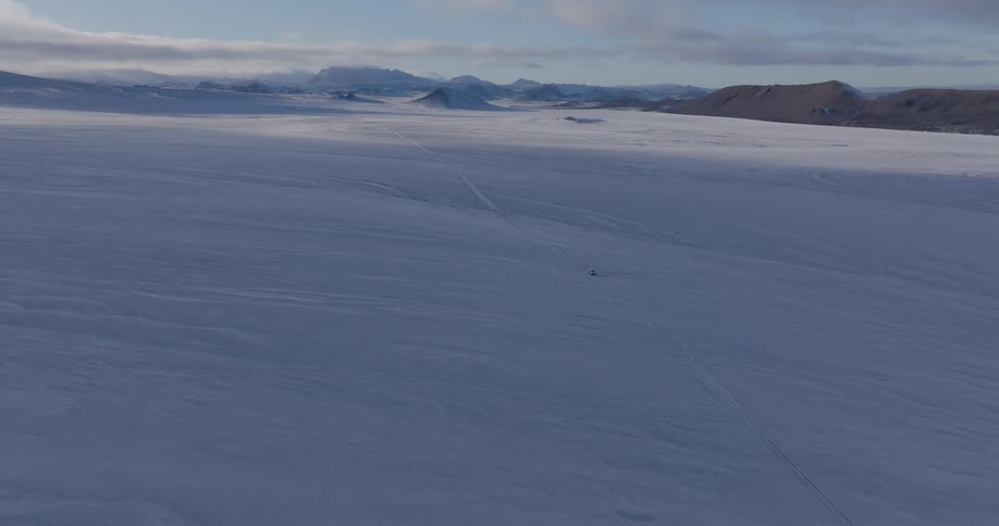An aerial view of a frozen landscape with mountains in the background in the daytime