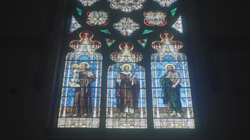 Perspective from below a tall stained glass church window depicting three saints