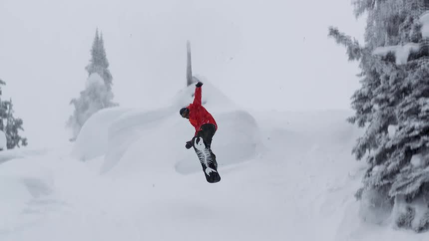 Snowboarder jumps and spins while tapping top of a tree into steep powder