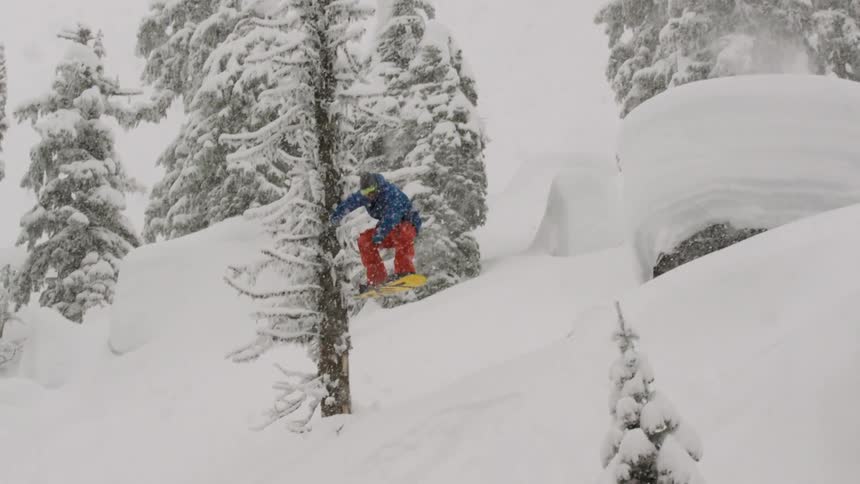 A snowboarder spins into powder over pillows in the backcountry