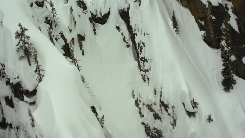 An aerial view of a man snowboarding down a steep snow covered mountain chute