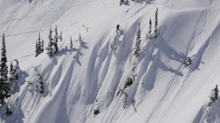 Aerial of snowboarder jumping and spinning into backcountry powder