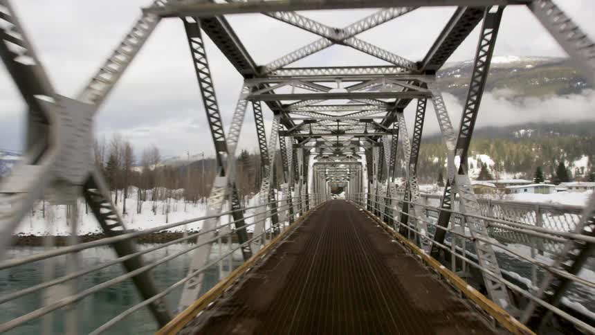 A bridge that passes over a river and the environment around it is trees and snow