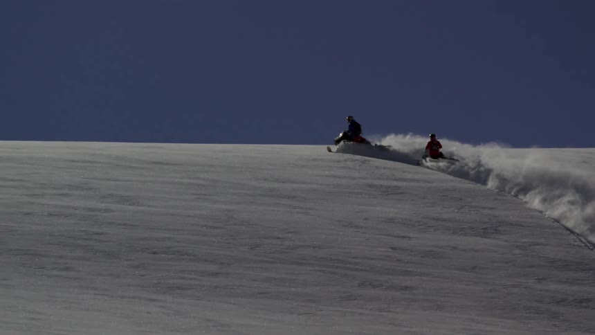 Two snowmobilers ride in deep powder on a sunny day