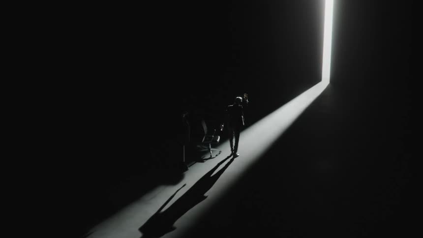 A man in a completely dark room walking towards the bright light coming in through a narrow opening