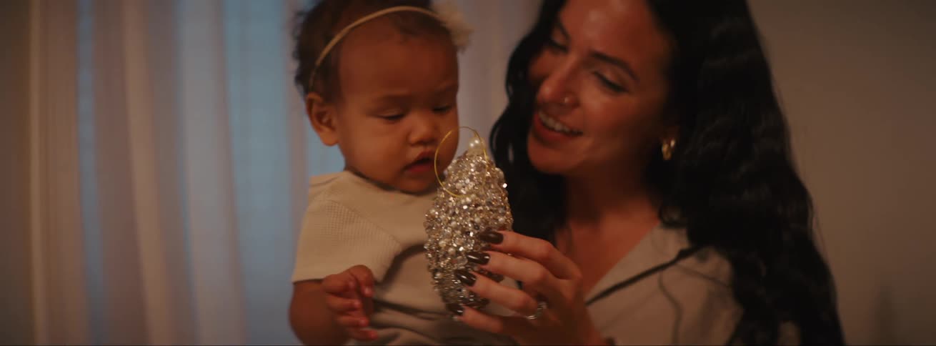 Mother holding her daughter in her arms and showing her a christmas ornament