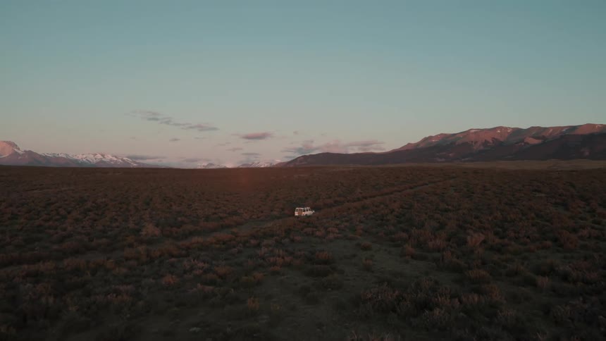 White car drives through the plains next to the mountains