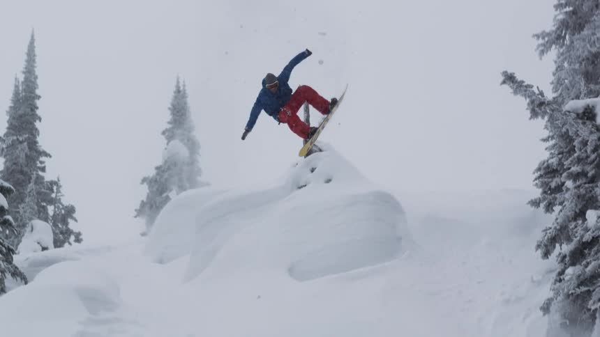 Snowboarder in the backcountry jumps and spins into powder