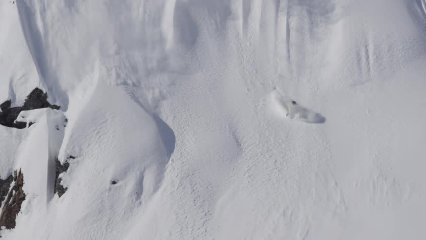 A snowboarder jumps and spins of a cliff in the sun