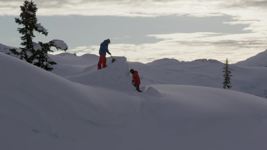 Two snowboarders building a jump in remote mountains