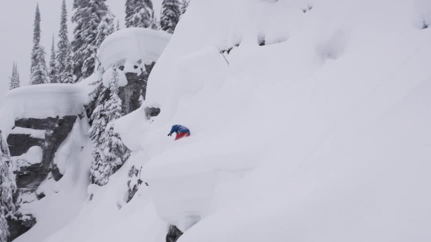 A snowboarder shreds through powder and trees