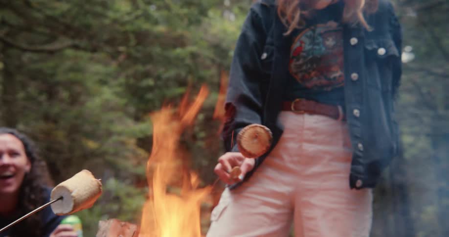 Girls around a campfire roasting marshmallows talking and laughing in the woods