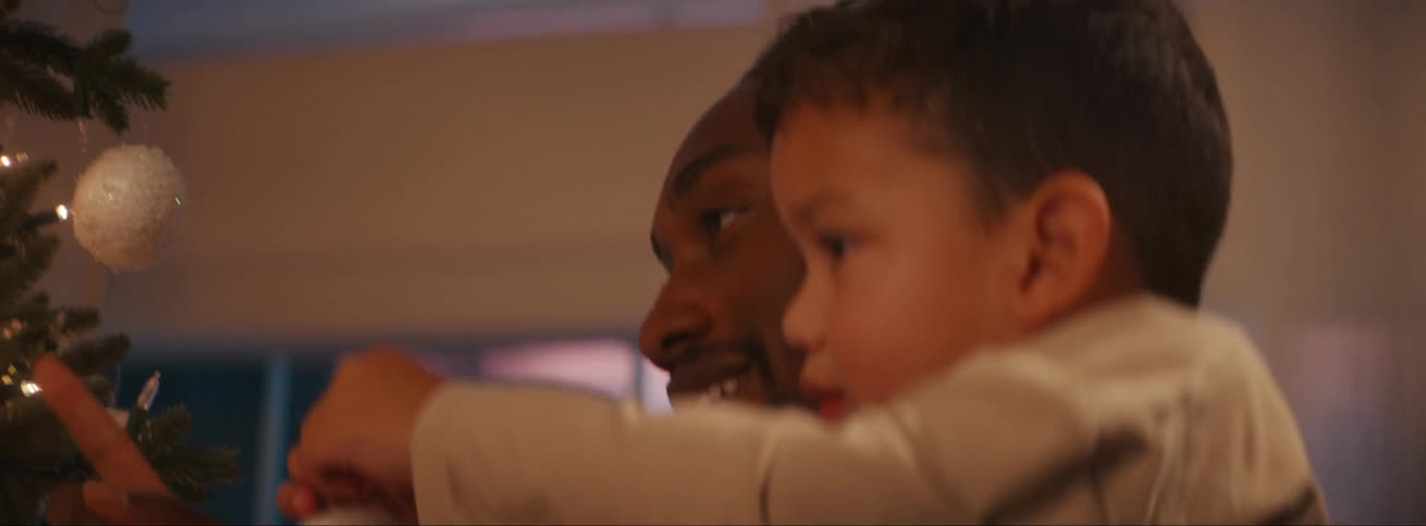 A father lifting his son to help him put a christmas decoration on the top of the christmas tree in the living room