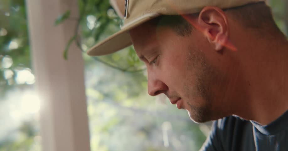 Profile view of a mans face wearing a baseball cap looking downward
