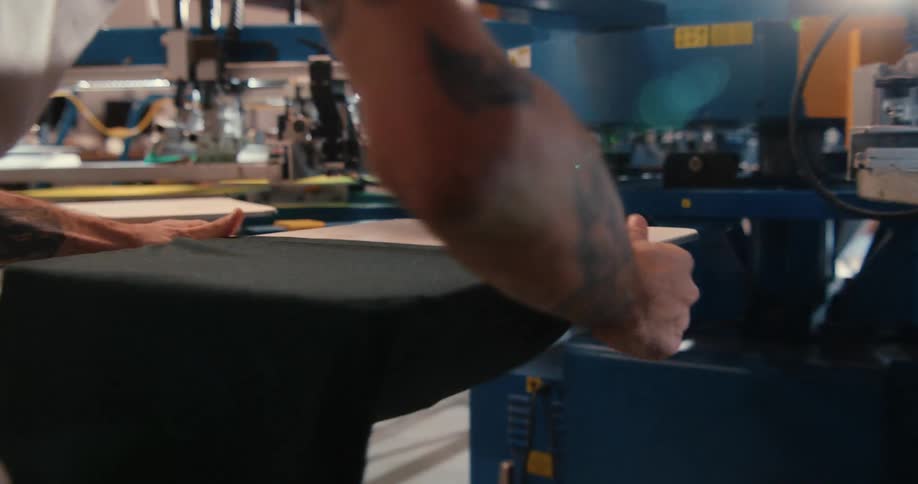 A man is working at a large workstation of machines in a tshirt printing company