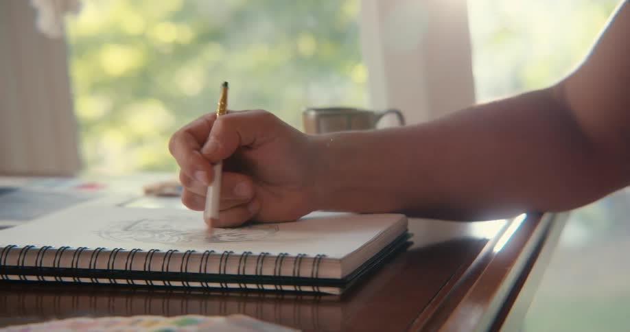 Person sketching on a book indoor with a pencil