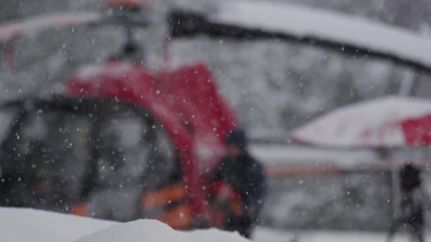 Snow falls as a helicopter pilot prepares his machine