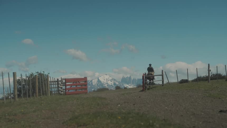 A man riding a horse out of a wooden fence during the day