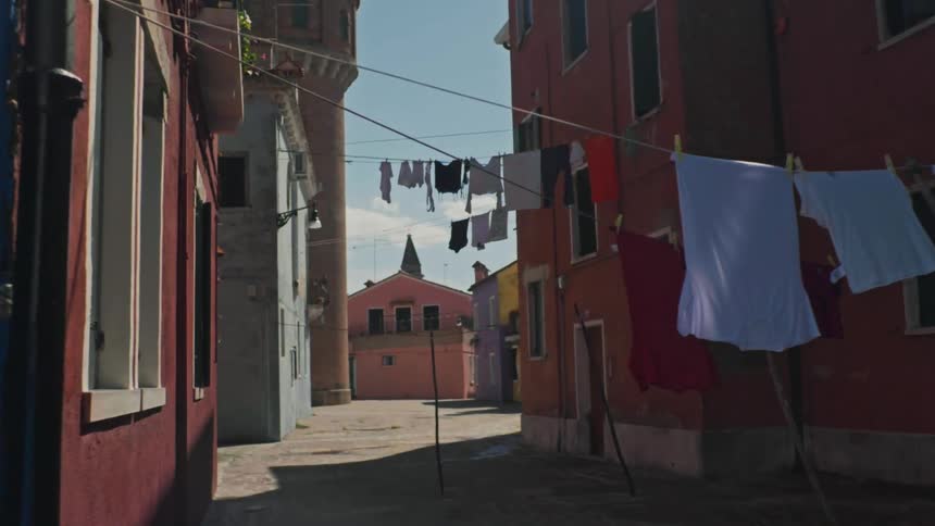 Clothes hang on lines strung between two colorful buildings in an unpaved alleyway of a spanish town shaded from the midday sun