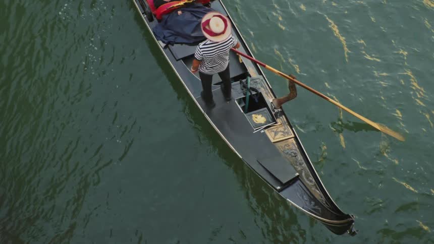 A standing gondolier steering the gondola through the canal while tourists are seated enjoying the ride