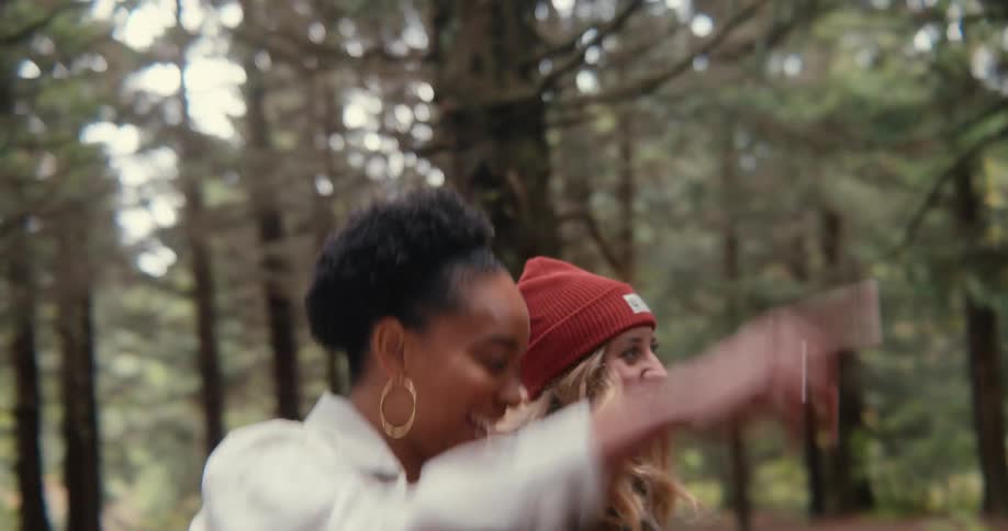 Two young women walk through a forest and laugh together
