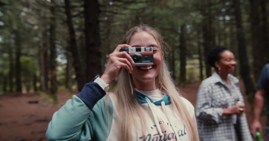 Portrait of a young blonde woman in the forest smiling and taking a photo with a camera