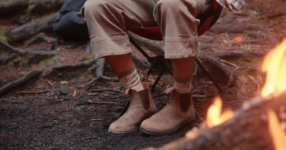 Legs of someone sitting near a burning fire in the woods at midday